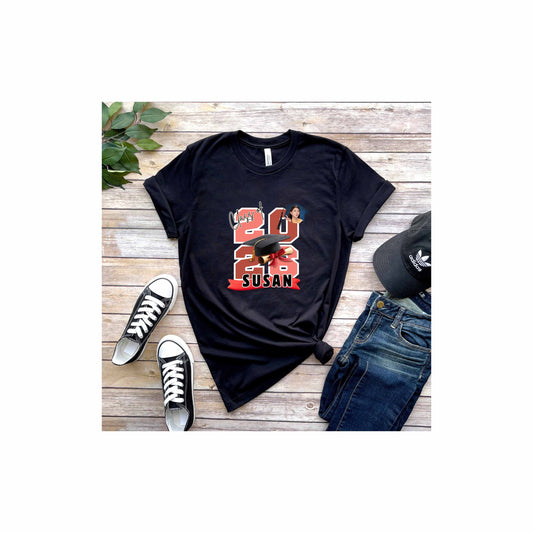 Black t-shirt with featuring the graduate's name, custom photo, graduation year, and classic cap-and-diploma artwork with graduation design and '2026 Susan' design on a wooden surface with shoes and jeans.