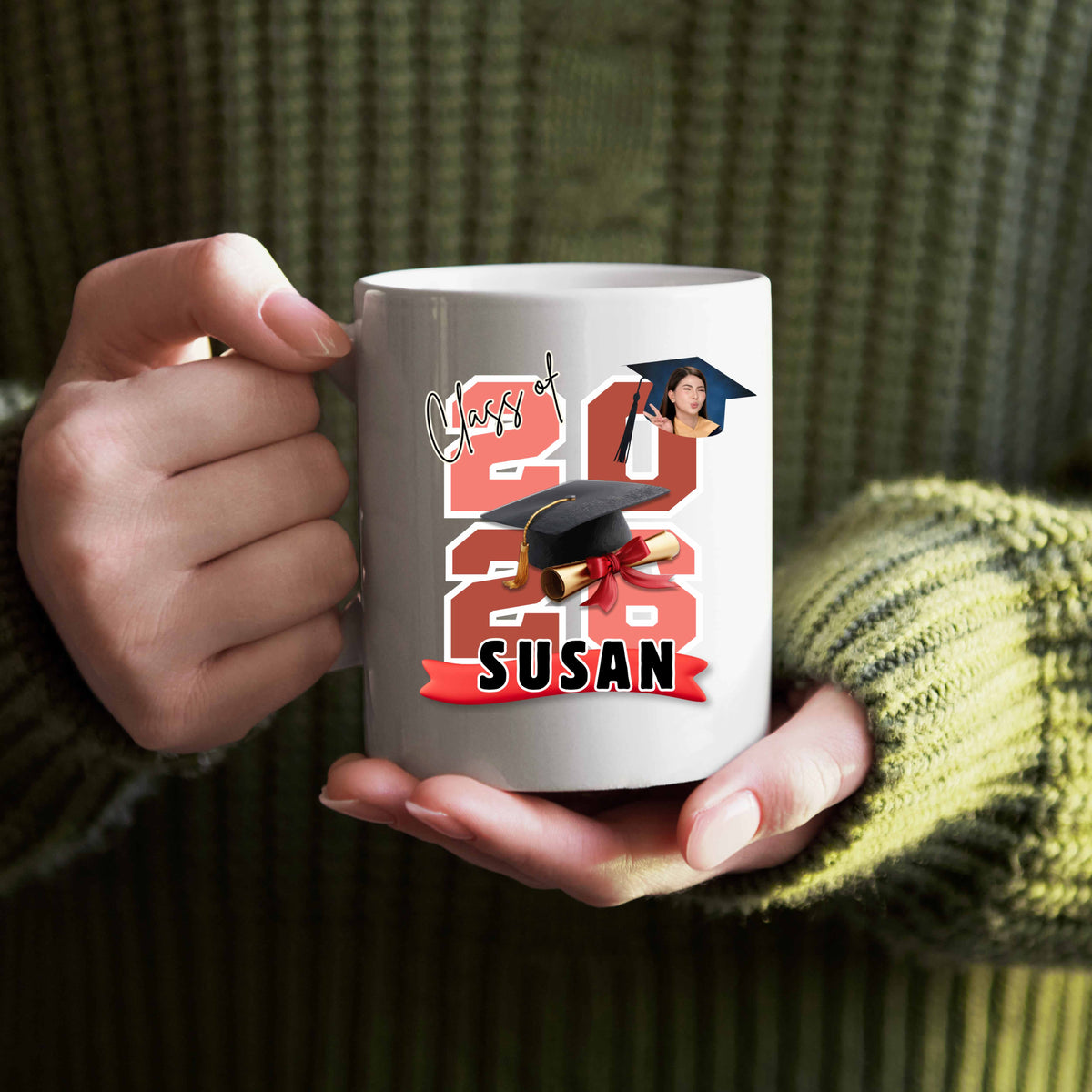Woman wearing a green sweater holding a white mug featuring the graduate's name, custom photo, graduation year, and classic cap-and-diploma artwork with graduation design and '2026 Susan' design