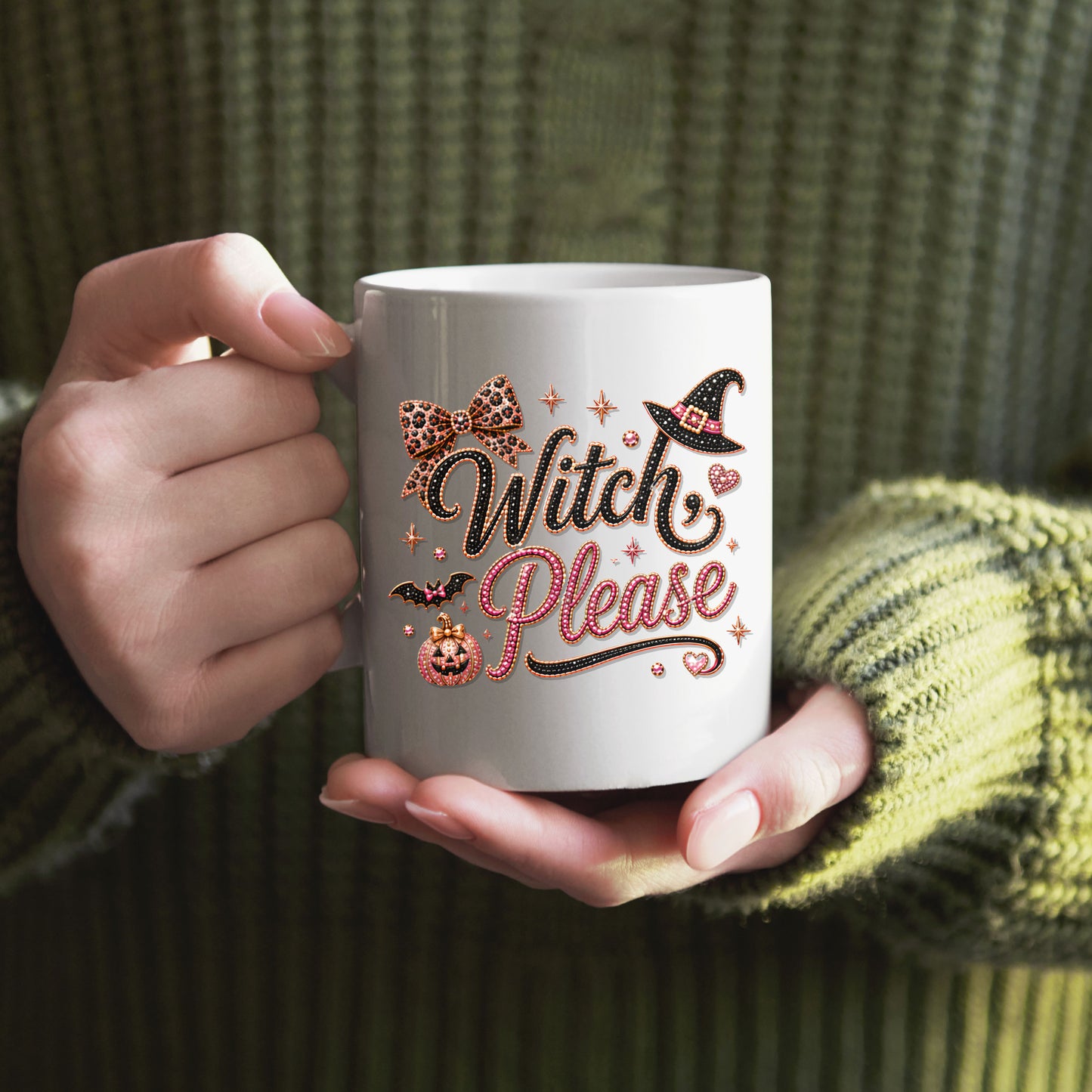 A person in a green ribbed sweater holds a white ceramic mug with a glittery 'Witch Please' Halloween design featuring a witch hat, pumpkin, and bow.