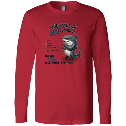 A men's long-sleeve crewneck t-shirt in red, featuring a graphic print of a shark with crossed arms and the text 'YOU CALL IT OCD I CALL IT.' along with a checklist and the phrase 'PUT THE TRICKS BACK WHERE I HAD THEM!' on a transparent