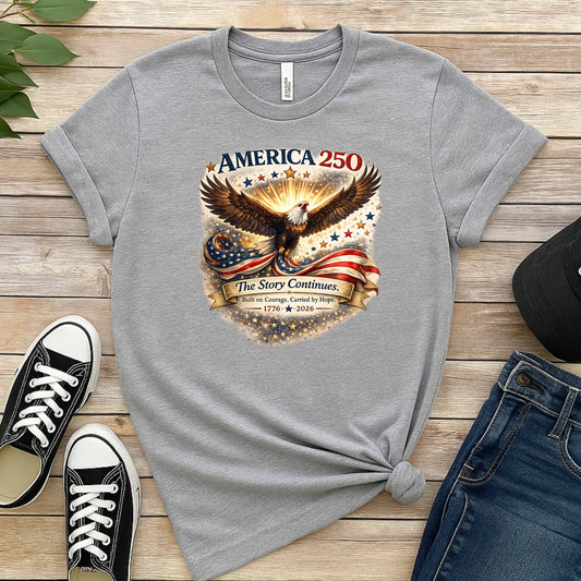 Gray t-shirt with eagle and American flag design on a wooden surface with shoes and jeans.