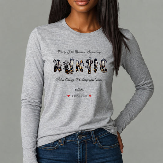 A woman wearing a heather gray long-sleeve t-shirt with a graphic print that reads 'Party Girls Become Legendary' and 'Auntie' in a floral and champagne -print pattern, paired with blue jeans against a solid gray background.