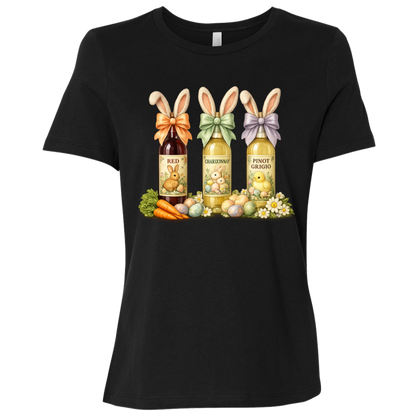 Image of a Black t-shirt with a colorful graphic design of three wine bottles (Red, Chardonnay, Pinot Grigio) with bows around the neck of the bottle and bunny ears posed in different positions at the top, flowers, a bunch of carrots and easter designed eggs are at the bottom surrounding the bottoms.