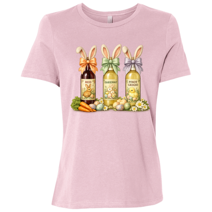 Image of a Pink t-shirt with a colorful graphic design of three wine bottles (Red, Chardonnay, Pinot Grigio) with bows around the neck of the bottle and bunny ears posed in different positions at the top, flowers, a bunch of carrots and easter designed eggs are at the bottom surrounding the bottoms.