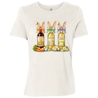 Image of a Vintage White t-shirt with a colorful graphic design of three wine bottles (Red, Chardonnay, Pinot Grigio) with bows around the neck of the bottle and bunny ears posed in different positions at the top, flowers, a bunch of carrots and easter designed eggs are at the bottom surrounding the bottoms.