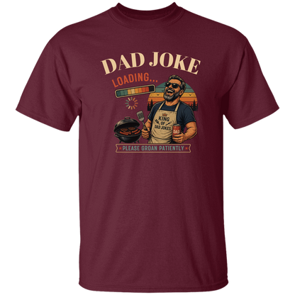 Maroon t-shirt "Dad Joke, Please Groin Patiently" featuring a retro-inspired grilling dad in sunglasses, a vintage sunset backdrop, and a playful loading bar graphic on a gray and black checkerboard background