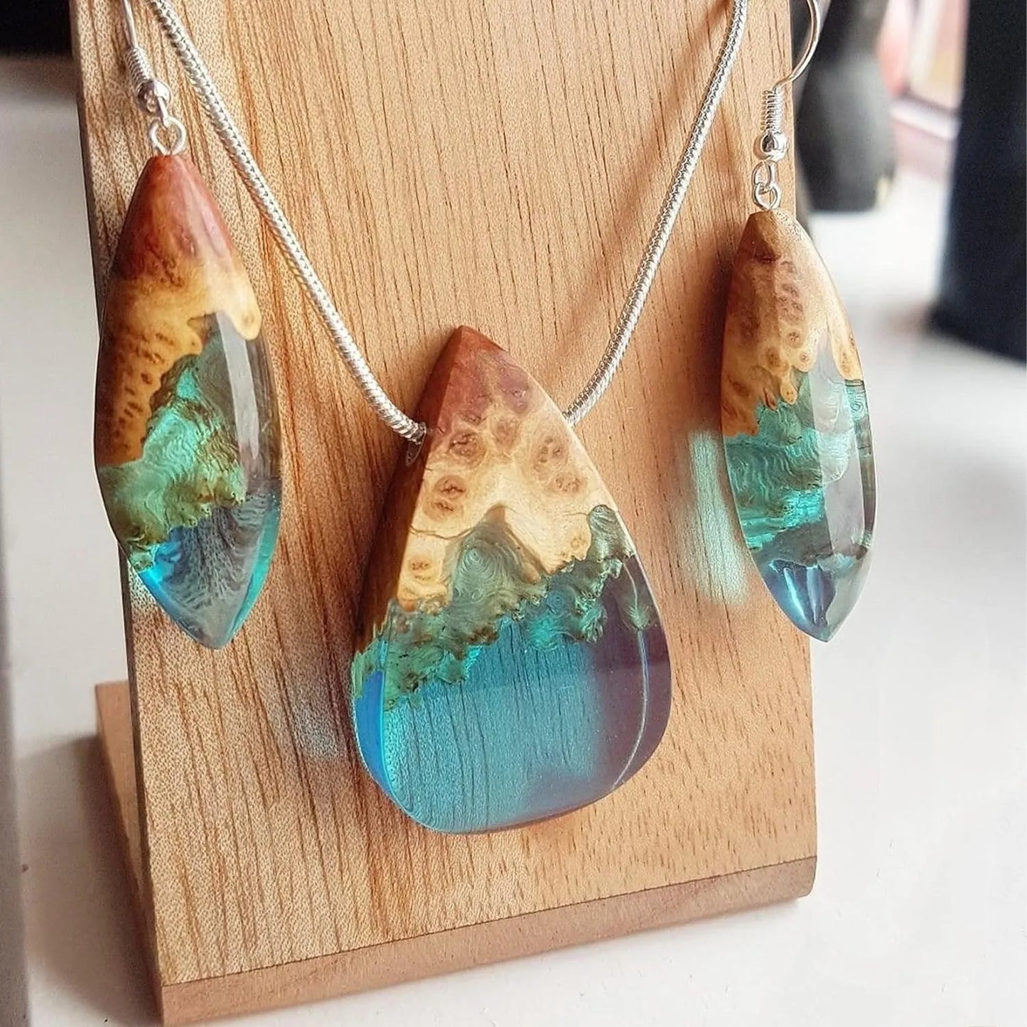 Wooden earrings and necklace with blue and green resin on a wooden stand.