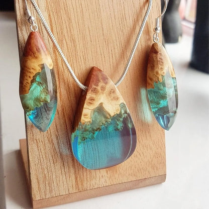 Wooden earrings and necklace with blue and green resin on a wooden stand.