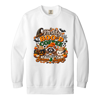 White Halloween coffee design sweatshirt featuring a cozy raccoon in an orange knit hat and scarf surrounded by pumpkin spice drinks, pumpkins, bats, and autumn leaves, with the text “Freshly Boo'd Coffee” and “Scream & Sugar” on a transparent background