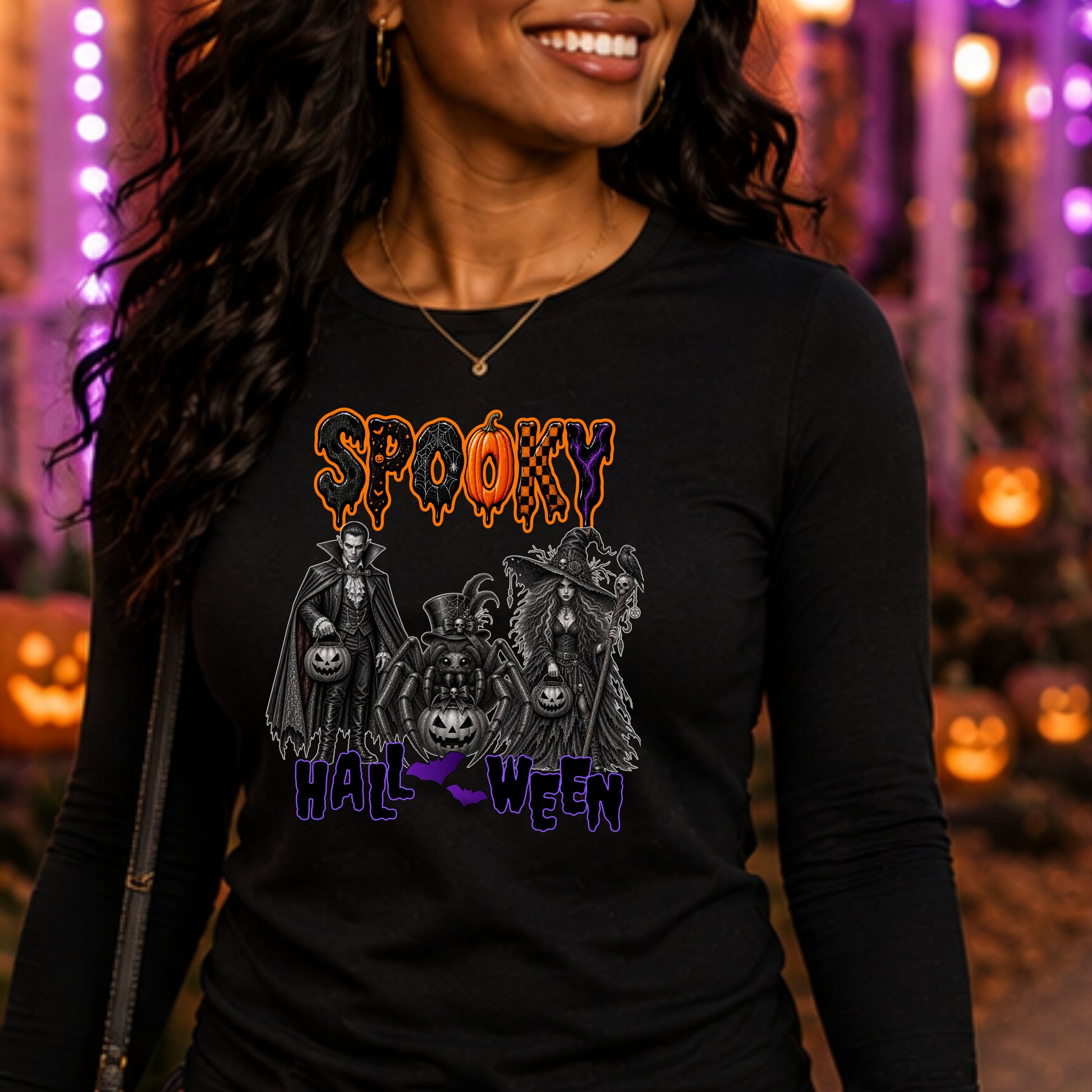 A woman wearing a black long-sleeve t-shirt with a 'Spooky Halloween' graphic print, set against a festive, blurred Halloween background with orange pumpkins and purple lights.