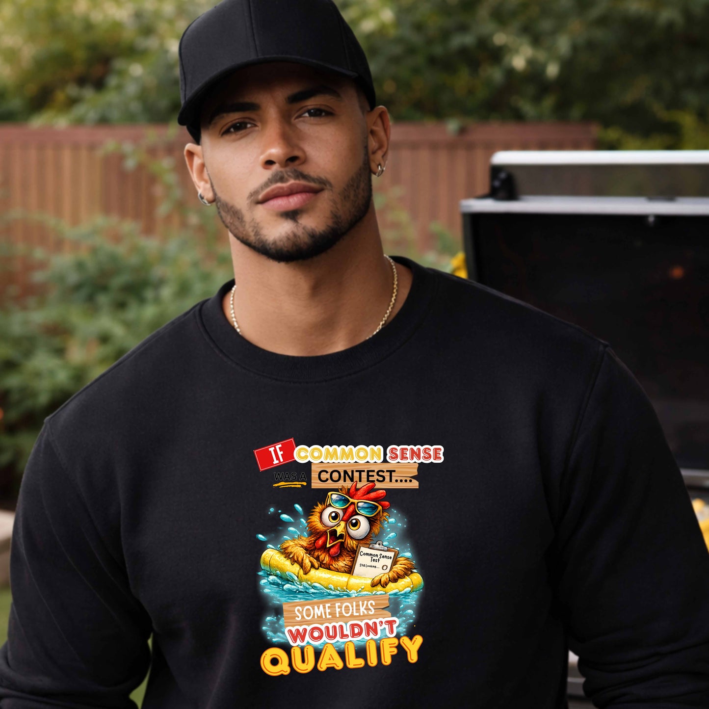 Man wearing a black long sleeve shirt with a graphic design and text with a colorful graphic and text featuring a wide-eyed pool-floating chicken desperately searching for common sense standing in a yard in front of a BBQ grill