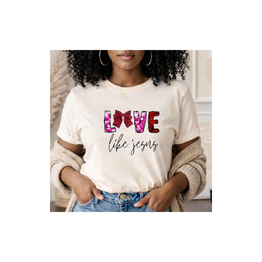 Woman wearing a white t-shirt with 'LOVE life Jesus' "Love Like Jesus" t-shirt featuring a stunning bow integrated into the word LOVE, standing in a neutral indoor setting.