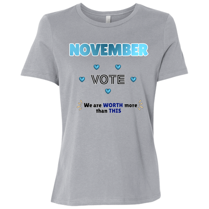 Bold November voting design on a Athletic Grey T-Shirt featuring large blue gradient “NOVEMBER” lettering at the top, surrounded by blue heart accents. The center features outlined “VOTE” text, while the bottom reads “We are WORTH more than THIS,” with WORTH and THIS highlighted in blue and warm gold decorative accents on both sides. The design has a transparent background and high-contrast outlined typography set on a transparent background