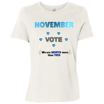 Bold November voting design on a Vintage White T-Shirt featuring large blue gradient “NOVEMBER” lettering at the top, surrounded by blue heart accents. The center features outlined “VOTE” text, while the bottom reads “We are WORTH more than THIS,” with WORTH and THIS highlighted in blue and warm gold decorative accents on both sides. The design has a transparent background and high-contrast outlined typography set on a transparent background