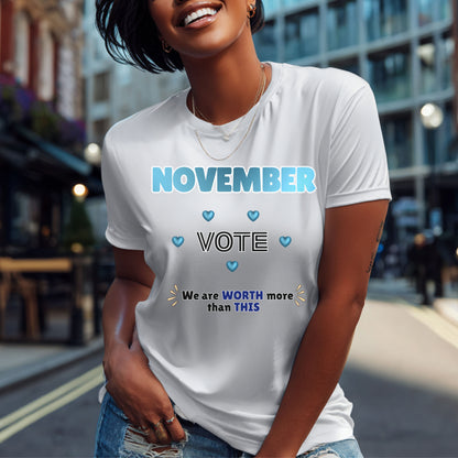 A woman wearing a white graphic t-shirt with the text 'NOVEMBER VOTE' and 'We are WORTH more than THIS' printed in blue and black, set against a blurred city street background.