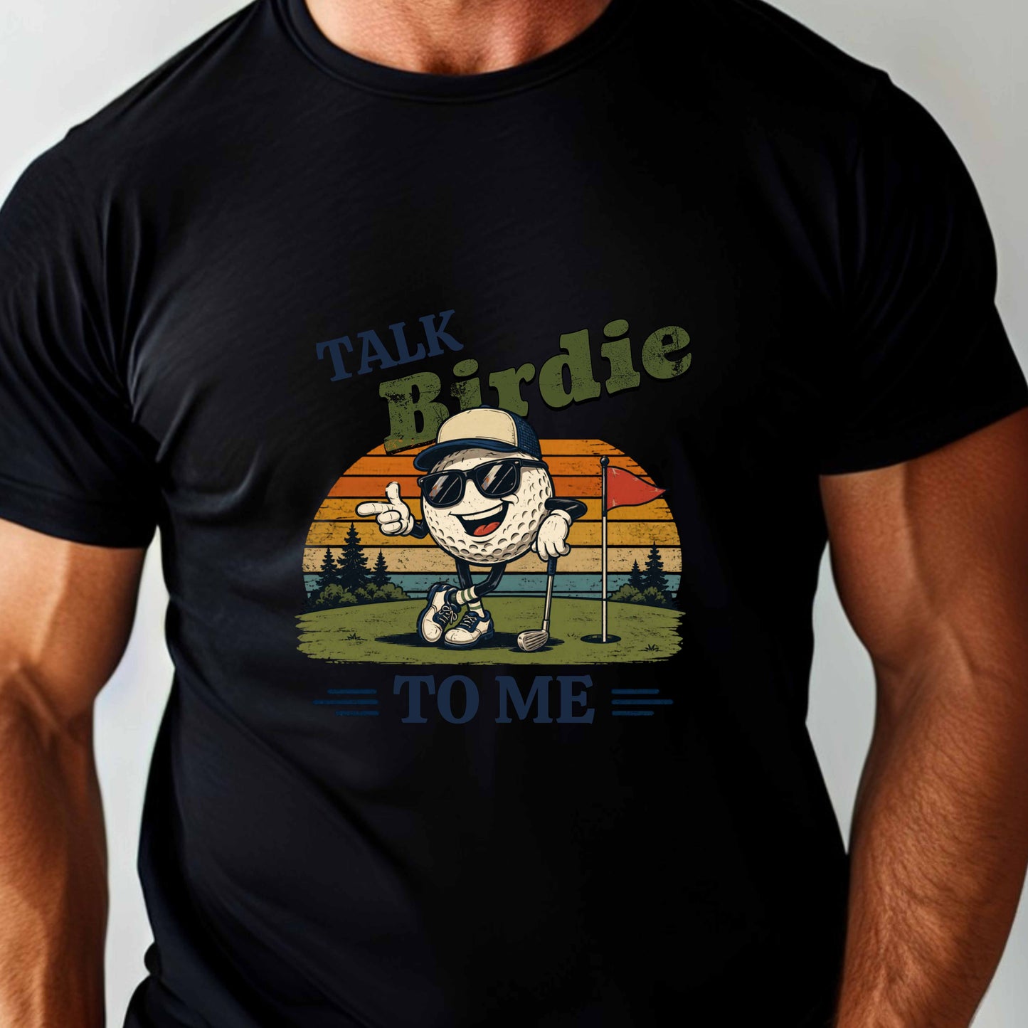 Muscular man wearing a black t-shirt with a graphic design and text "Talk Birdie To Me" t-shirt featuring a cool cartoon golf ball rocking sunglasses on the green  leaning on a golf club and next to a putting hole with a flag inside of the hole with  a retro sunset background