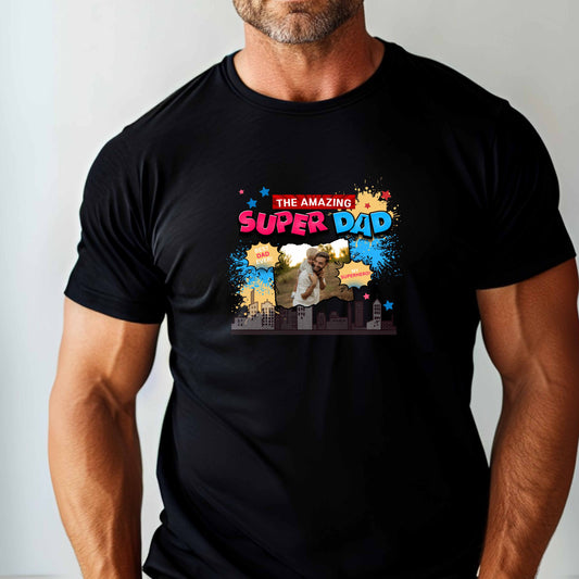 Black t-shirt with 'The Amazing Super Dad' graphic and featuring eye-catching pop art elements, city skyline graphics, comic-style bursts, and a personalized photo placement of a man and child on a plain background