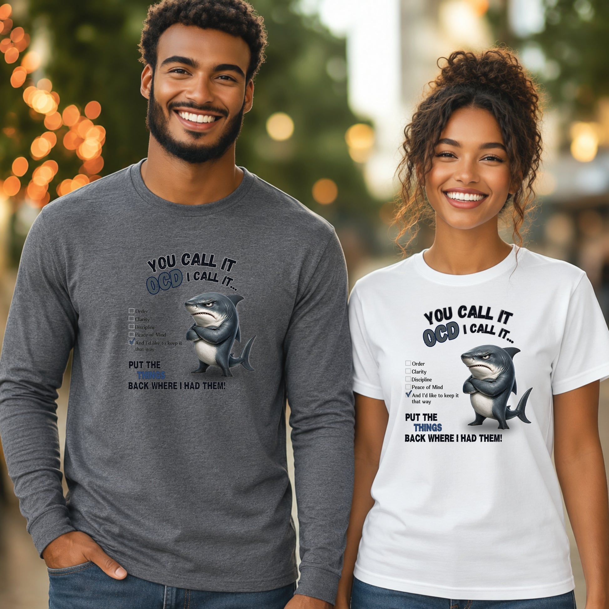 Two smiling adults standing outdoors wearing matching graphic long-sleeve shirts. The shirt design shows a shark illustration with the text 'YOU CALL IT OCD.