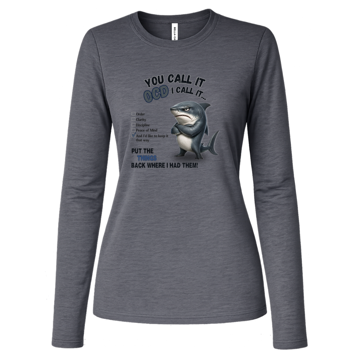 A women's long-sleeve crewneck t-shirt in deep heather, featuring a graphic print of a shark with crossed arms and the text 'YOU CALL IT OCD I CALL IT.' along with a checklist and the phrase 'PUT THE TRICKS BACK WHERE I HAD THEM!' on a transparent background
