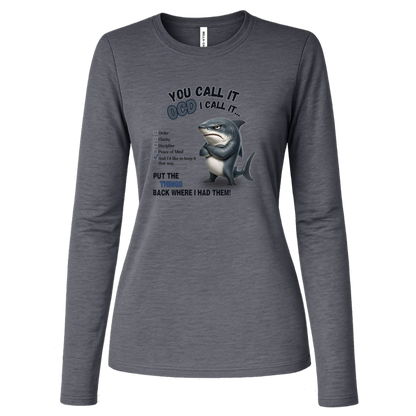 A women's long-sleeve crewneck t-shirt in deep heather, featuring a graphic print of a shark with crossed arms and the text 'YOU CALL IT OCD I CALL IT.' along with a checklist and the phrase 'PUT THE TRICKS BACK WHERE I HAD THEM!' on a transparent background