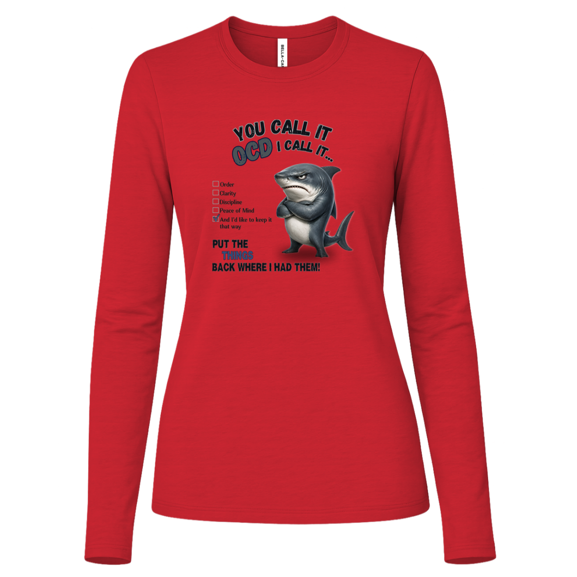 A women's long-sleeve crewneck t-shirt in red, featuring a graphic print of a shark with crossed arms and the text 'YOU CALL IT OCD I CALL IT.' along with a checklist and the phrase 'PUT THE TRICKS BACK WHERE I HAD THEM!' on a transparent background