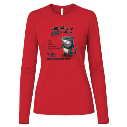 A women's long-sleeve crewneck t-shirt in red, featuring a graphic print of a shark with crossed arms and the text 'YOU CALL IT OCD I CALL IT.' along with a checklist and the phrase 'PUT THE TRICKS BACK WHERE I HAD THEM!' on a transparent background