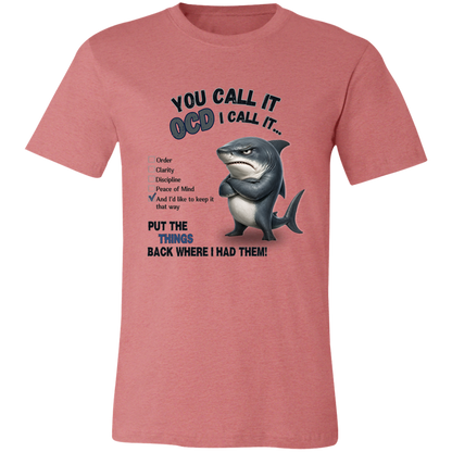 A unisex t-shirt in heather mauve, featuring a graphic print of a shark with crossed arms and the text 'YOU CALL IT OCD I CALL IT.' along with a checklist and the phrase 'PUT THE TRICKS BACK WHERE I HAD THEM!' on a transparent 