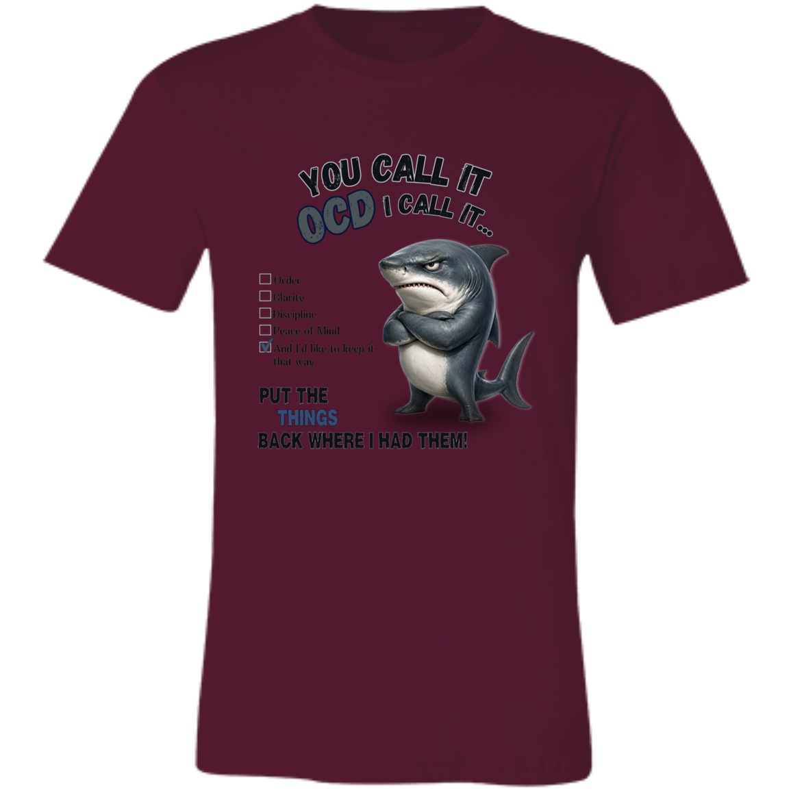 A unisex t-shirt in maroon, featuring a graphic print of a shark with crossed arms and the text 'YOU CALL IT OCD I CALL IT.' along with a checklist and the phrase 'PUT THE TRICKS BACK WHERE I HAD THEM!' on a transparent 