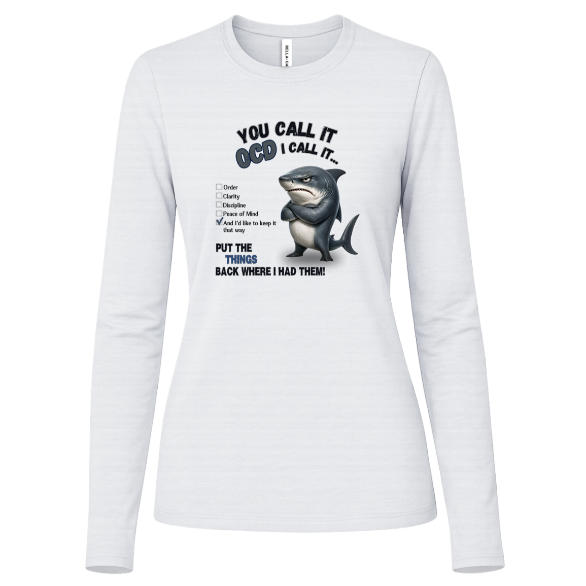 A women's long-sleeve crewneck t-shirt in white, featuring a graphic print of a shark with crossed arms and the text 'YOU CALL IT OCD I CALL IT.' along with a checklist and the phrase 'PUT THE TRICKS BACK WHERE I HAD THEM!' on a transparent background