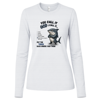 A women's long-sleeve crewneck t-shirt in white, featuring a graphic print of a shark with crossed arms and the text 'YOU CALL IT OCD I CALL IT.' along with a checklist and the phrase 'PUT THE TRICKS BACK WHERE I HAD THEM!' on a transparent background