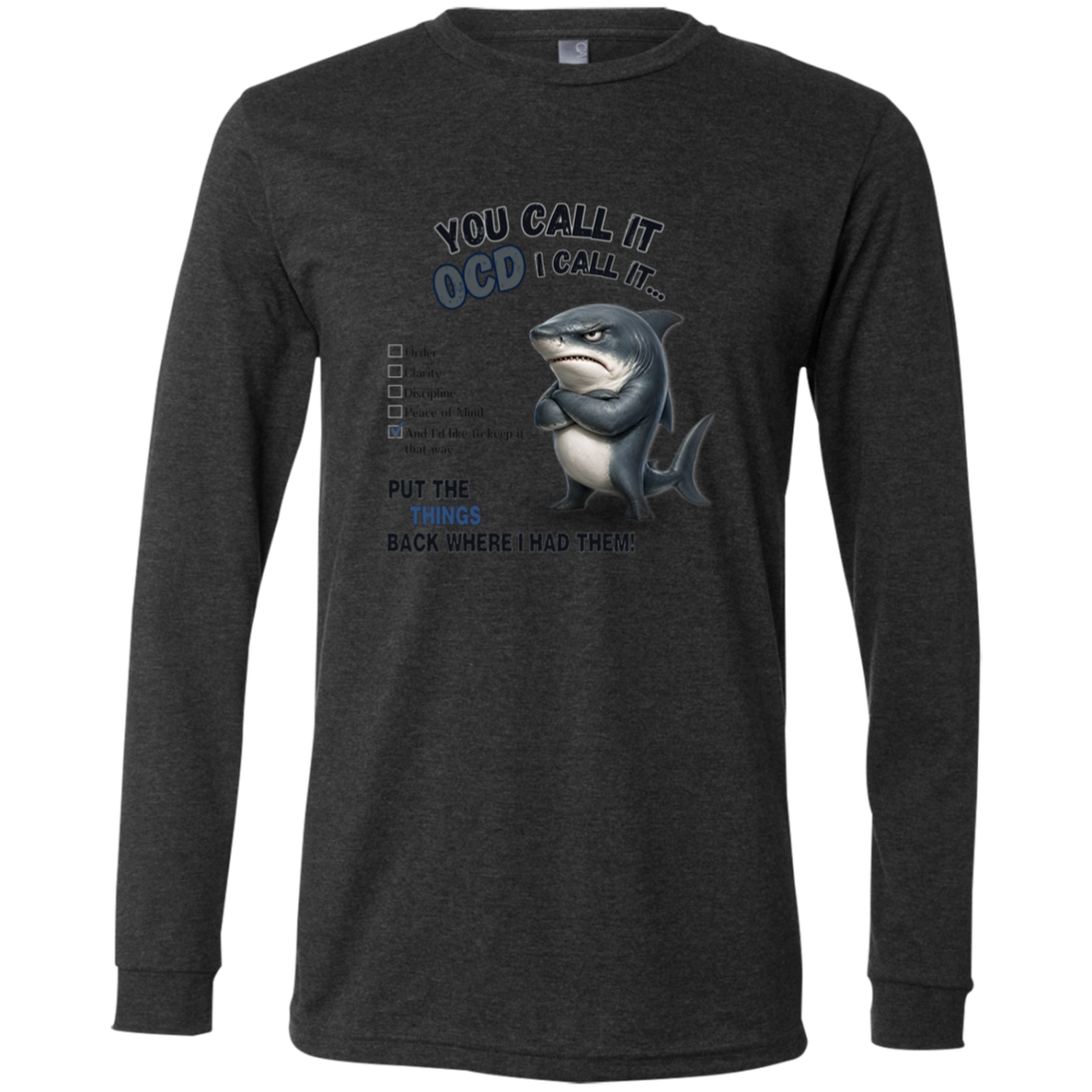 A men's long-sleeve crewneck t-shirt in dark grey heather, featuring a graphic print of a shark with crossed arms and the text 'YOU CALL IT OCD I CALL IT.' along with a checklist and the phrase 'PUT THE TRICKS BACK WHERE I HAD THEM!' on a transparent 