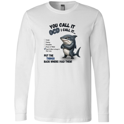 A men's long-sleeve crewneck t-shirt in white, featuring a graphic print of a shark with crossed arms and the text 'YOU CALL IT OCD I CALL IT.' along with a checklist and the phrase 'PUT THE TRICKS BACK WHERE I HAD THEM!' on a transparent 